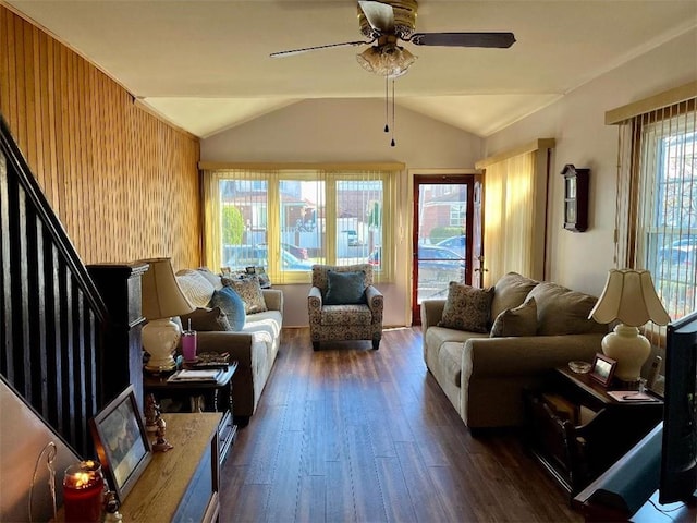 living room featuring lofted ceiling, wooden walls, a ceiling fan, stairs, and dark wood finished floors