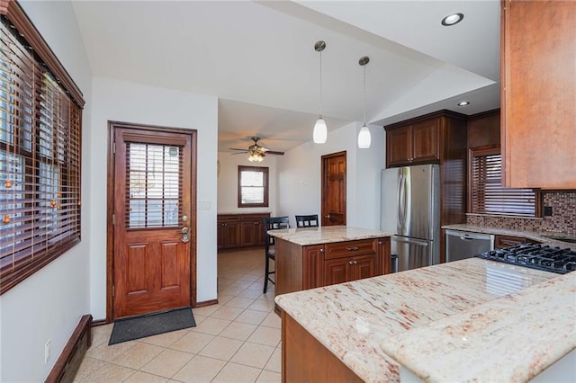 kitchen with appliances with stainless steel finishes, light stone counters, decorative light fixtures, a center island, and lofted ceiling