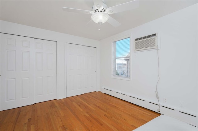 unfurnished bedroom with a wall unit AC, two closets, a baseboard radiator, a ceiling fan, and wood finished floors