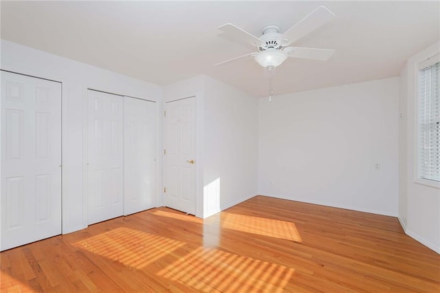 unfurnished bedroom featuring multiple closets, ceiling fan, and hardwood / wood-style floors