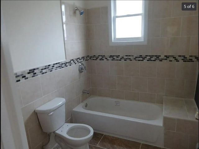 bathroom with tile patterned floors, tiled shower / bath combo, toilet, and tile walls