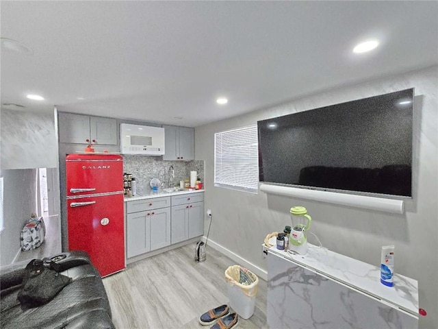 kitchen with light wood-type flooring, backsplash, sink, and gray cabinetry