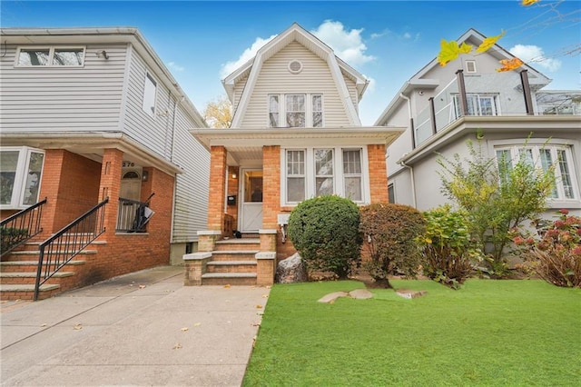 view of front of property featuring a gambrel roof, a front lawn, entry steps, a balcony, and brick siding