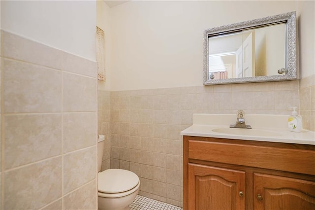 bathroom featuring tile walls, toilet, tile patterned floors, vanity, and a wainscoted wall