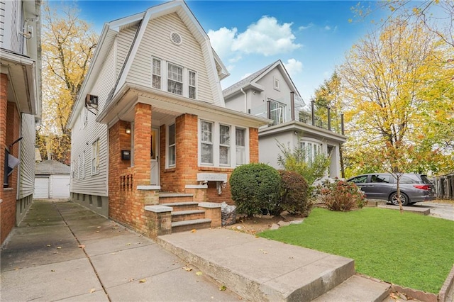 dutch colonial featuring a garage, brick siding, a front yard, and a gambrel roof