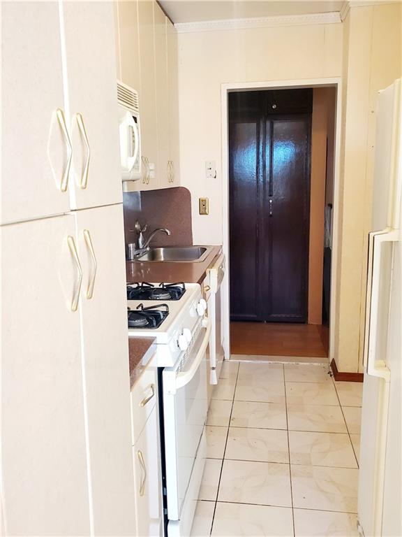 kitchen with crown molding, light countertops, white cabinets, a sink, and white appliances