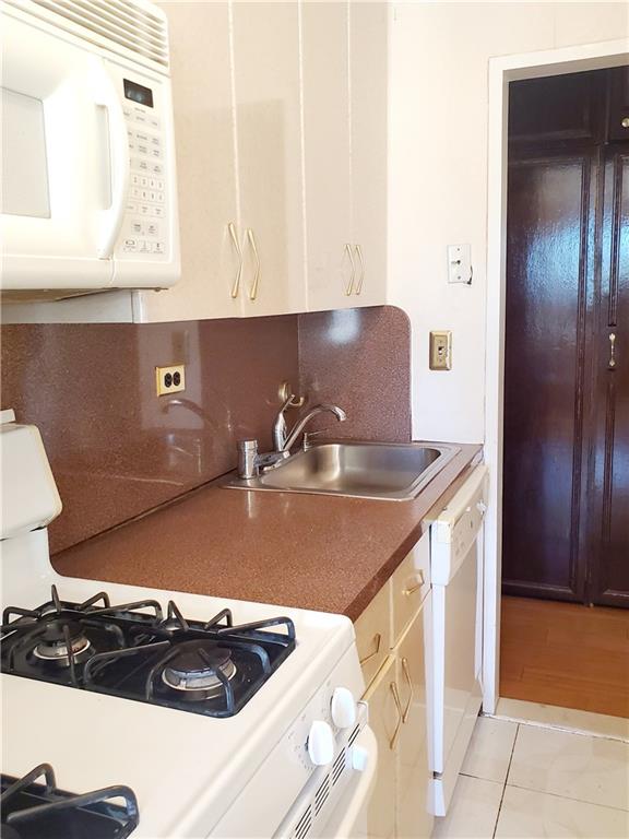 kitchen with light tile patterned floors, tasteful backsplash, white cabinetry, a sink, and white appliances