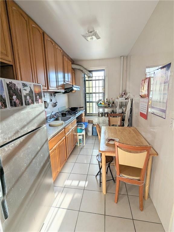 kitchen with stainless steel refrigerator, sink, light tile patterned floors, and extractor fan