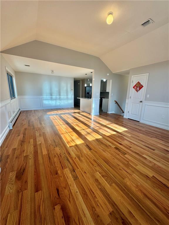 unfurnished living room with vaulted ceiling, baseboard heating, and light hardwood / wood-style flooring