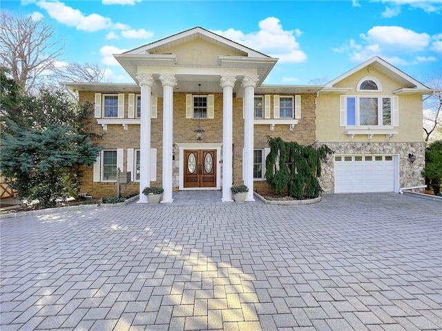 greek revival inspired property featuring stone siding, brick siding, decorative driveway, and an attached garage