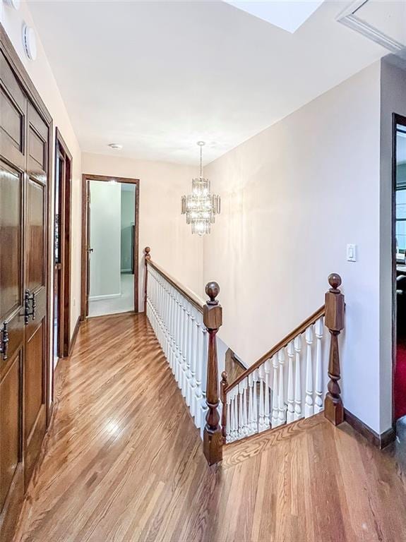 corridor with an inviting chandelier, light wood-style flooring, baseboards, and an upstairs landing