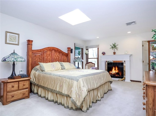 bedroom with a glass covered fireplace, visible vents, recessed lighting, light carpet, and a skylight