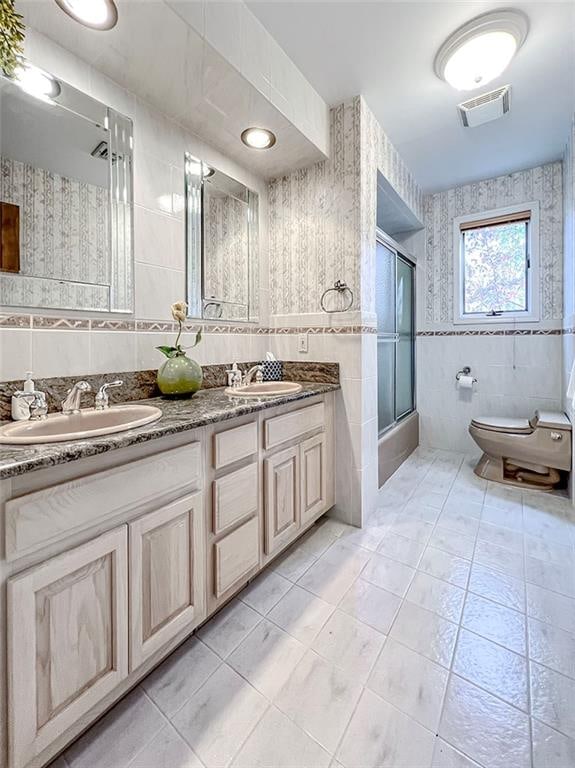 bathroom featuring a sink, wallpapered walls, visible vents, and tile walls