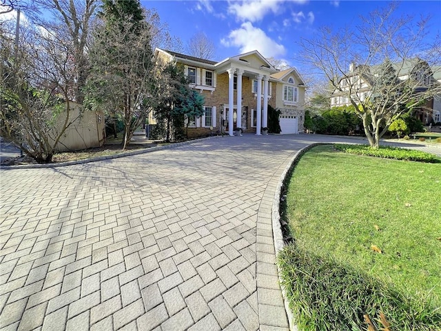 greek revival inspired property featuring an attached garage, decorative driveway, and a front yard