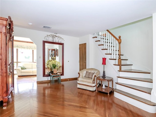 living area with arched walkways, visible vents, stairway, wood finished floors, and baseboards