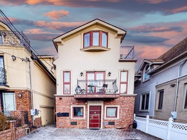 front of property at dusk with brick siding, stucco siding, a balcony, and fence