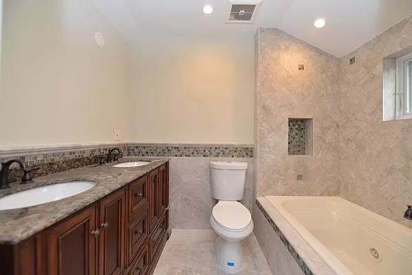 bathroom with tile walls, a tub to relax in, vanity, and toilet