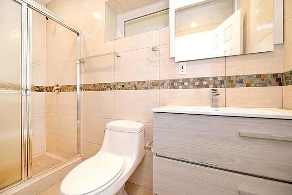 bathroom featuring vanity, toilet, a shower with door, and tile walls