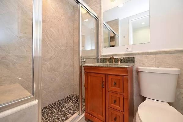 bathroom with vanity, tile walls, walk in shower, and toilet