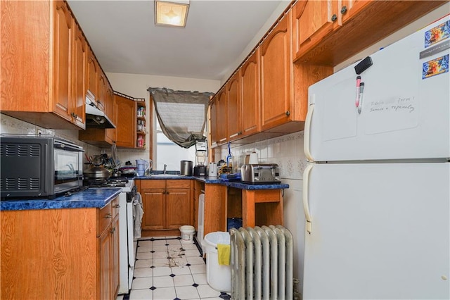 kitchen featuring gas range oven, radiator heating unit, brown cabinetry, freestanding refrigerator, and black microwave