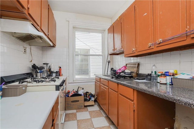 kitchen with brown cabinetry, backsplash, light floors, and white gas range