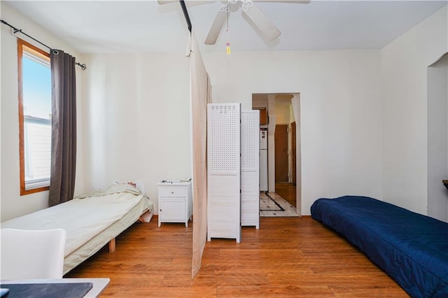 bedroom with freestanding refrigerator, ceiling fan, and light wood finished floors