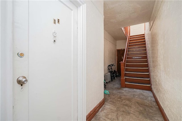 interior space featuring stairway, baseboards, a textured ceiling, and a textured wall