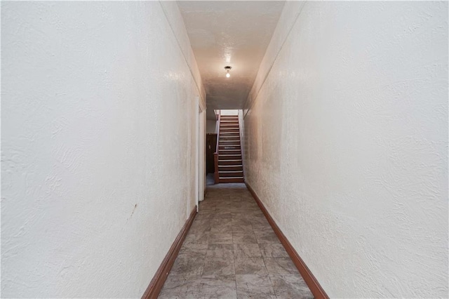 hallway with stairs, baseboards, and a textured wall