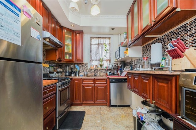 kitchen featuring a raised ceiling, glass insert cabinets, stainless steel appliances, under cabinet range hood, and backsplash