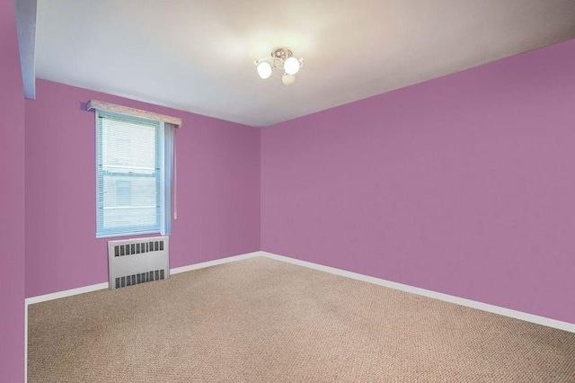 empty room featuring carpet flooring, radiator, and baseboards