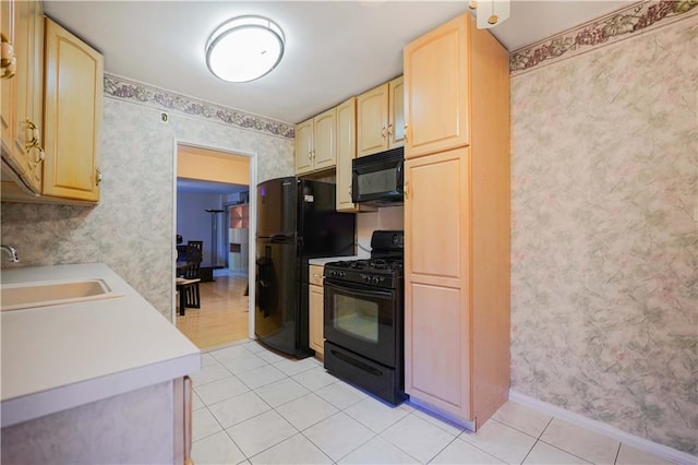 kitchen featuring black appliances, light brown cabinets, a sink, wallpapered walls, and light countertops