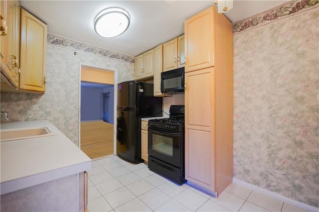 kitchen with black appliances, light brown cabinetry, a sink, wallpapered walls, and light countertops