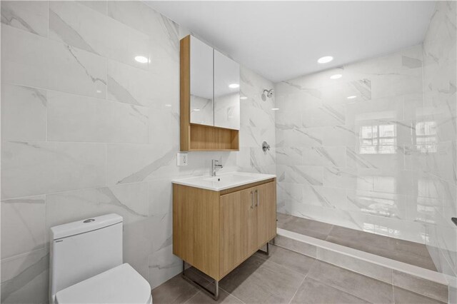 bathroom with tile patterned floors, tiled shower, toilet, vanity, and tile walls