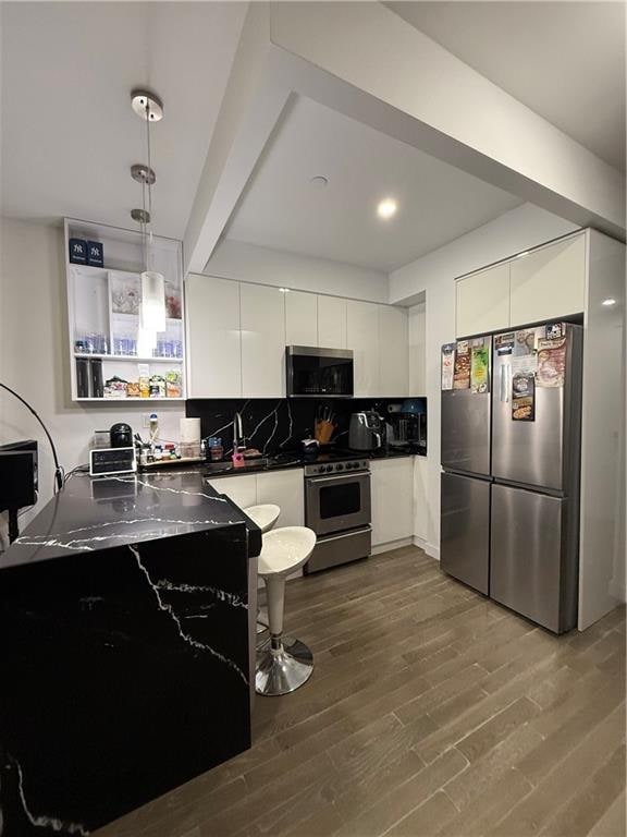 kitchen featuring white cabinets, tasteful backsplash, decorative light fixtures, wood-type flooring, and stainless steel appliances