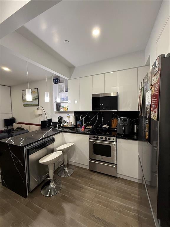 kitchen with decorative light fixtures, stainless steel appliances, white cabinetry, and dark wood-type flooring