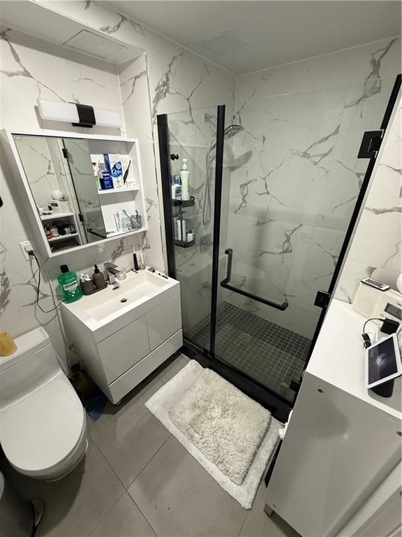 bathroom featuring vanity, toilet, a shower with shower door, and tile walls