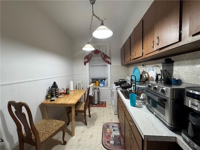 kitchen featuring white gas range, dark brown cabinets, pendant lighting, and sink