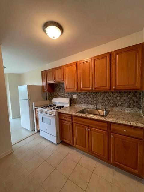 kitchen with sink, light stone counters, backsplash, white appliances, and light tile patterned floors