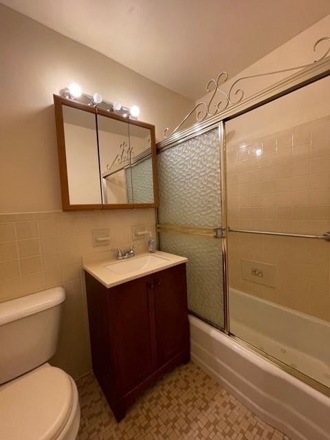 full bath featuring vanity, tile walls, toilet, and shower / bath combination with glass door