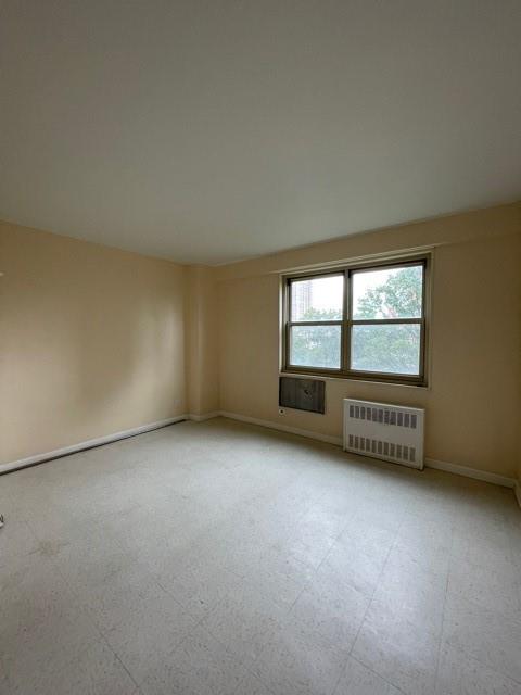 unfurnished room with light floors, radiator, and baseboards