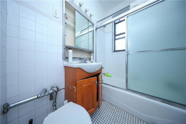 full bathroom with vanity, toilet, bath / shower combo with glass door, and tile walls