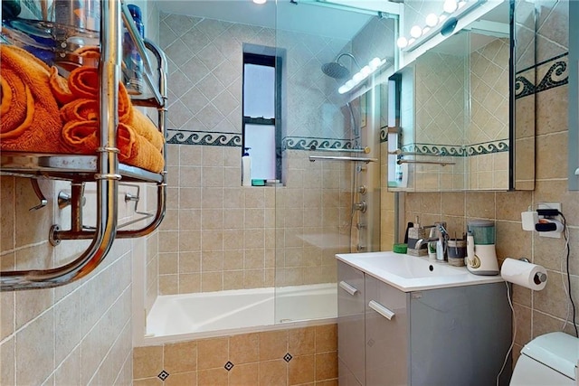 full bathroom featuring tiled shower / bath, vanity, toilet, and tile walls