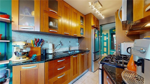 kitchen featuring sink, stainless steel fridge, dark stone counters, decorative backsplash, and light tile patterned floors