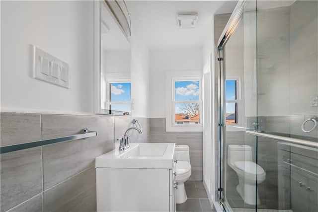 bathroom featuring a shower with door, tile walls, tile patterned flooring, vanity, and toilet