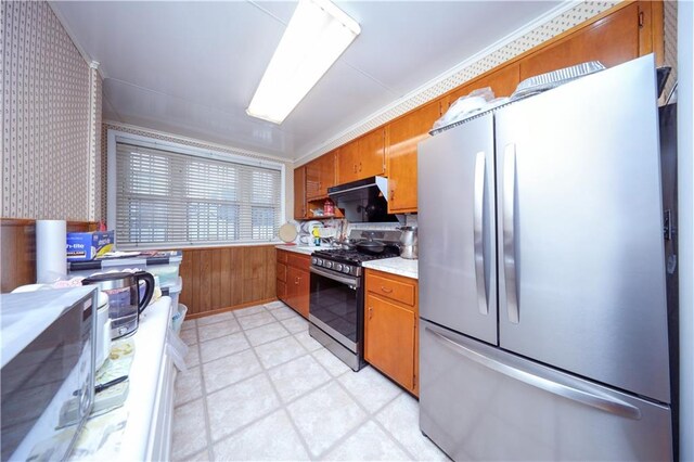 kitchen with black gas range oven, ornamental molding, stainless steel refrigerator, and wood walls