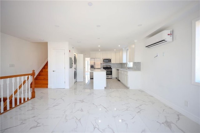 kitchen featuring stainless steel appliances, a wall mounted AC, a center island, stacked washer and dryer, and white cabinetry