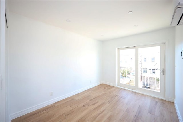 spare room featuring light wood-type flooring and an AC wall unit