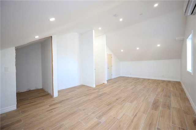 bonus room with vaulted ceiling, a wall mounted air conditioner, and light wood-type flooring