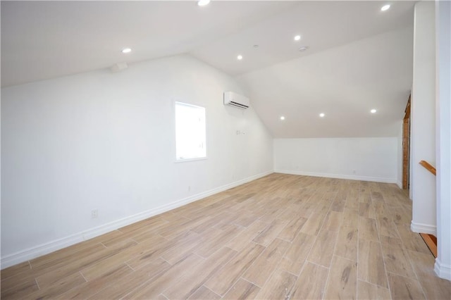 additional living space with a wall mounted air conditioner, vaulted ceiling, and light wood-type flooring