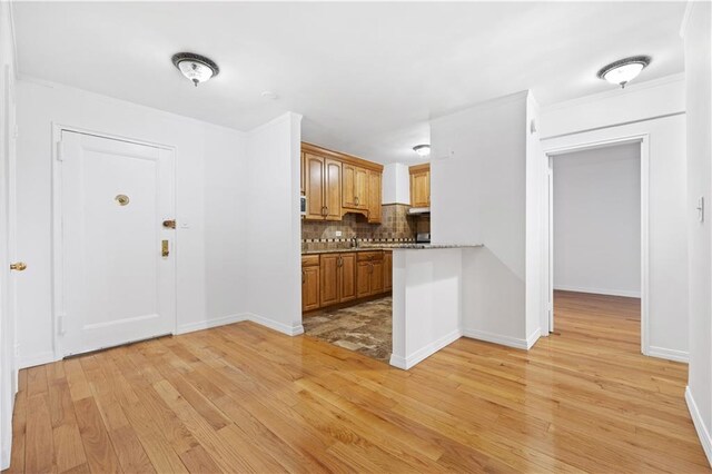 kitchen with kitchen peninsula, light wood-type flooring, tasteful backsplash, and light stone counters